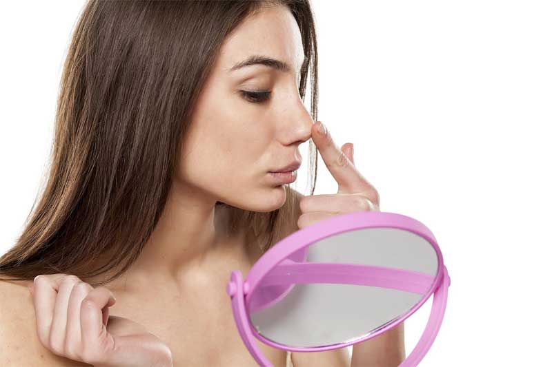 Mujer mirando su nariz en el espejo